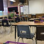 Rows of empty desks and chairs in a classroom with a whiteboard at the front