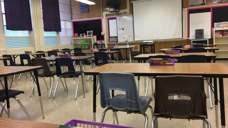 Rows of empty desks and chairs in a classroom with a whiteboard at the front