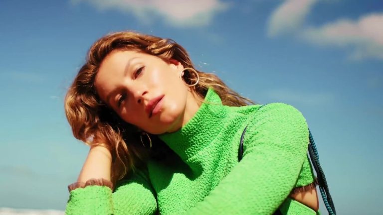 Gisele Bündchen in a green sweater, resting her head on her hand against a blue sky