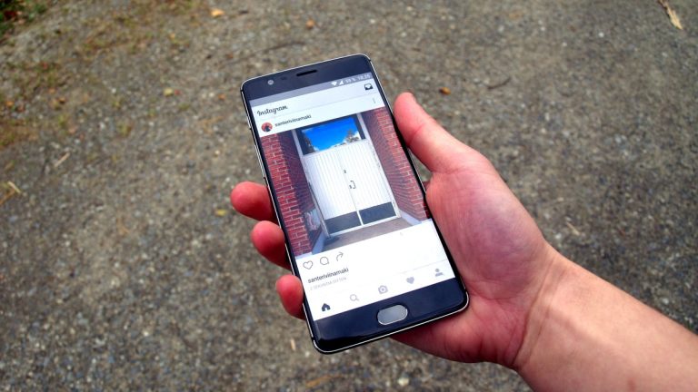 A hand holding a smartphone showing the Instagram app over a gravel background