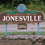 Welcome to Jonesville sign, chartered 1794, with a flower bed at its base beside a road in Lee County, Virginia