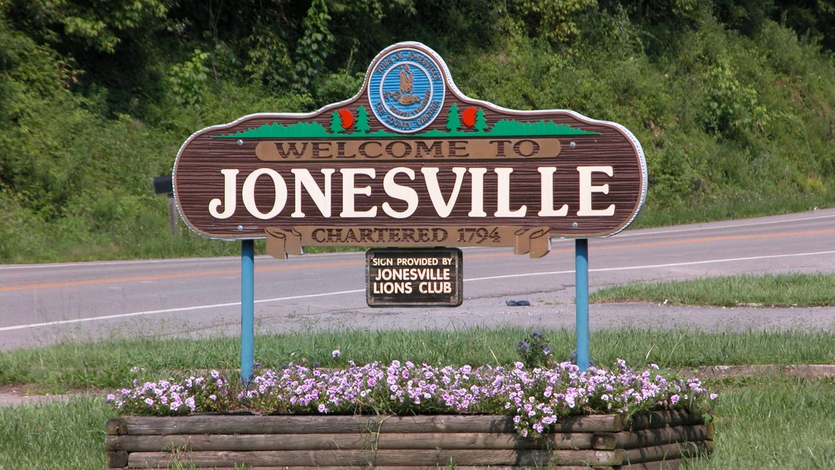 Welcome to Jonesville sign, chartered 1794, with a flower bed at its base beside a road in Lee County, Virginia