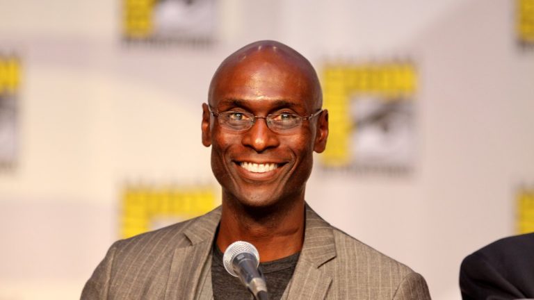 Lance Reddick smiling at a panel microphone at San Diego Comic-Con