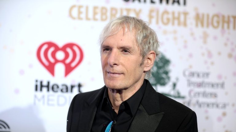 Singer Michael Bolton in a black suit on a red carpet in front of a sponsor backdrop