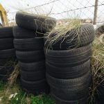 A pile of old tires stacked against a fence with grass growing on top