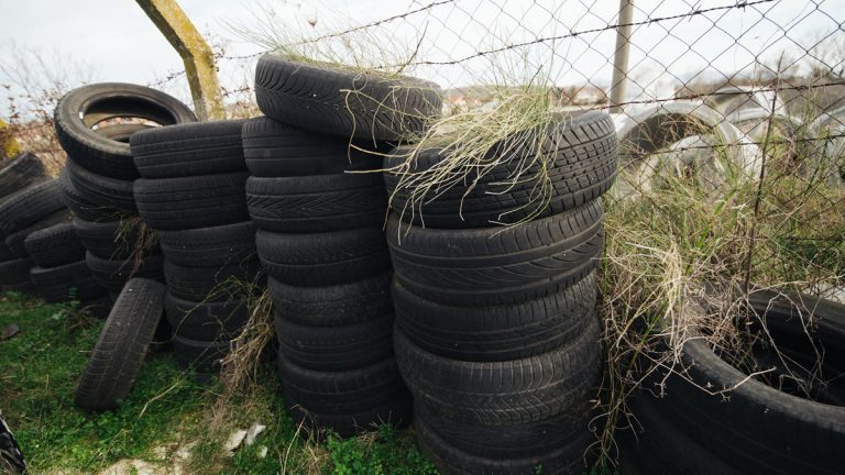 A pile of old tires stacked against a fence with grass growing on top