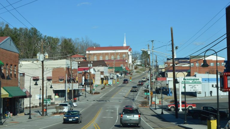 Morgan Avenue (U.S. Route 58 Alternate) running uphill through downtown Pennington Gap, with brick storefronts, a pharmacy sign and a church on the hill under a clear blue sky