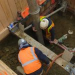 Two workers in a shored trench working on a sewer line