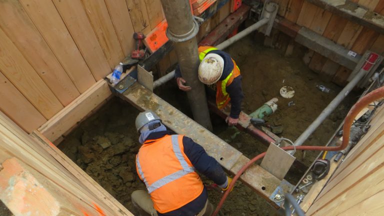 Two workers in a shored trench working on a sewer line