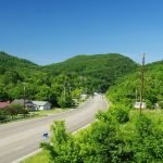 A four-lane stretch of U.S. Route 58 running between green hills past houses at Ben Hur in Lee County, Virginia