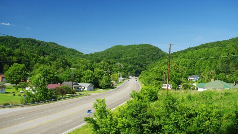 A four-lane stretch of U.S. Route 58 running between green hills past houses at Ben Hur in Lee County, Virginia