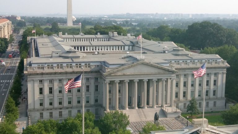 Aerial view of the U.S. Treasury building with American flags and the Washington Monument in the distance